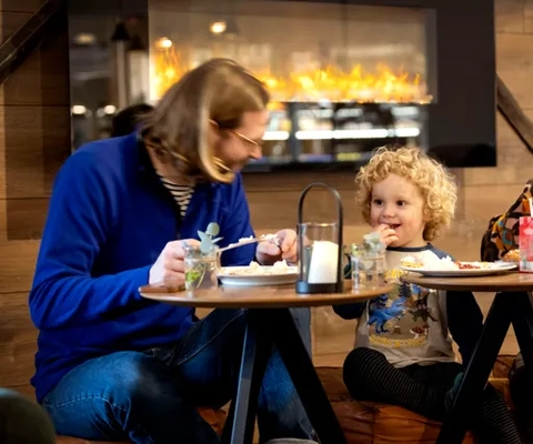 Pappa och son sitter framför brasan och äter och skrattar.