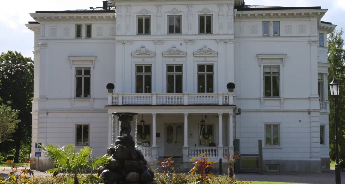 En stor vit byggnad med en fontän framför.