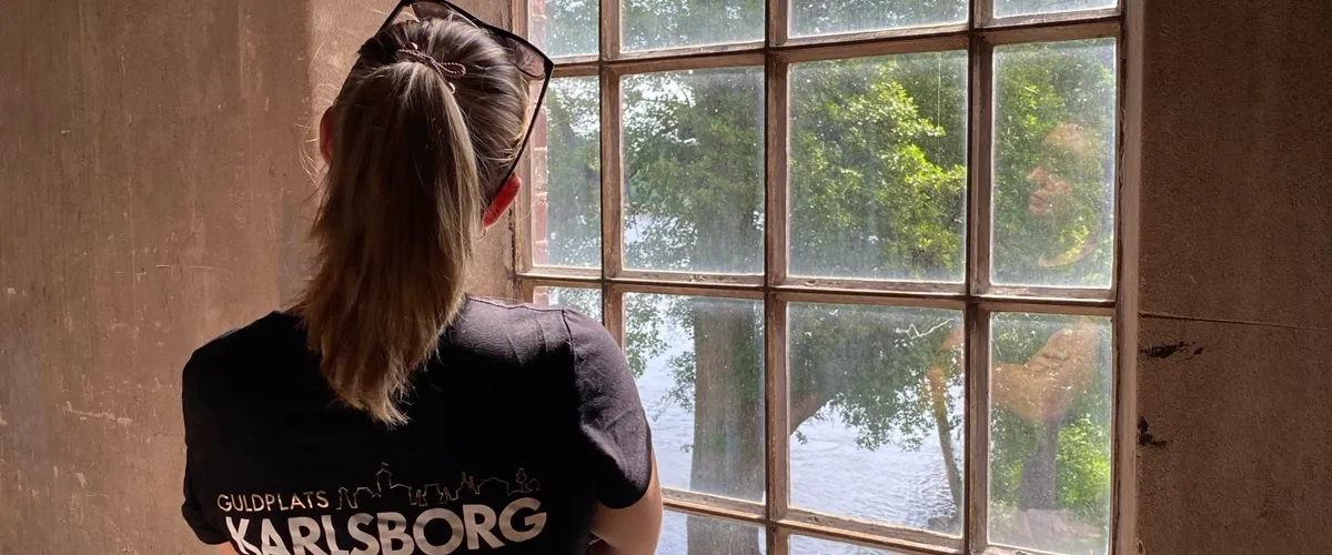 En kvinna står framför ett fönster och tittar ut.