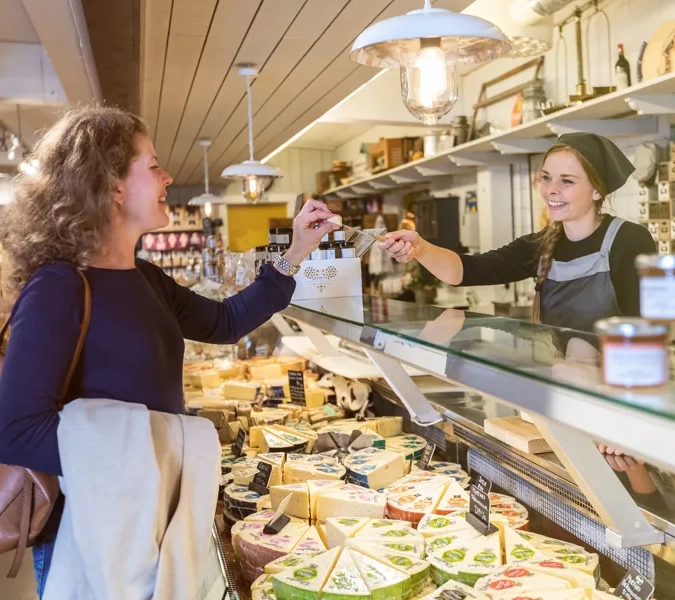 Kvinna som provsmakar en ostbit som expediten ger henne över en ostdisk.