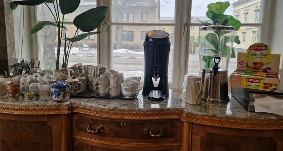 En kaffebryggare och koppar som står på en bänk bredvid ett fönster.