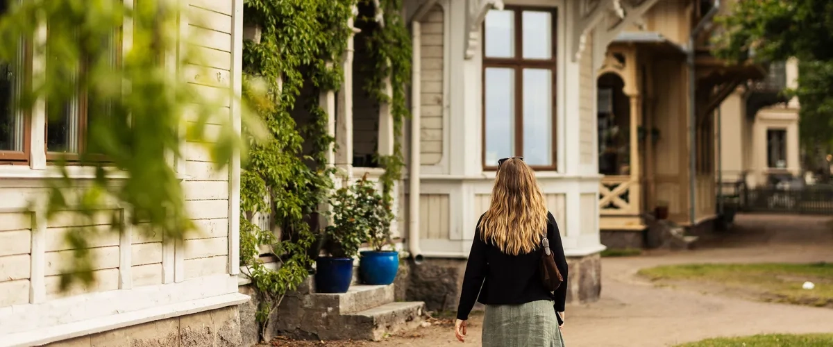 En kvinna går längs en grusväg framför ett hus.