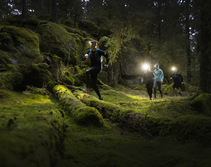 Four runners wearing headlamps run through a forest.