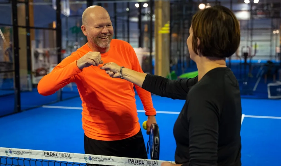 En man och en kvinna skakar hand över ett padelnät.