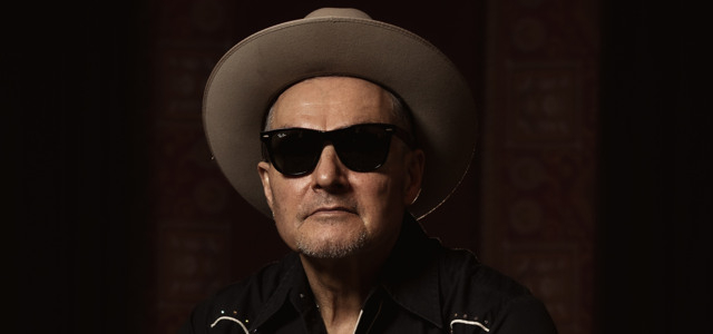 En man i cowboyhatt och solglasögon sitter i en stol.