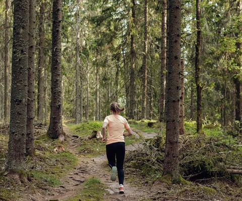 Eine Frau, die auf einem Pfad durch den Wald läuft.