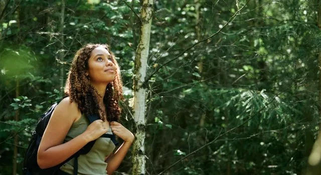 En person som står i skogen med en ryggsäck.