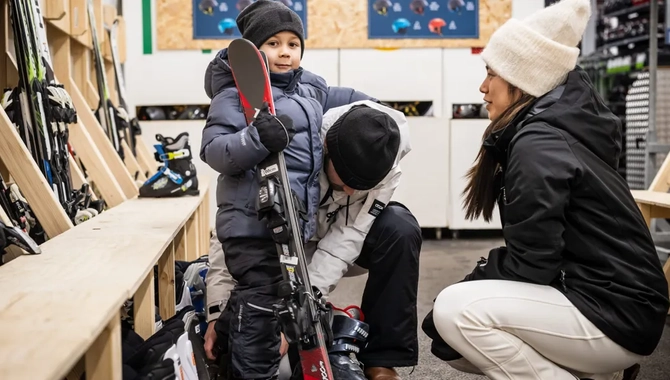 En kvinna knäböjer bredvid en liten pojke som håller i ett par skidor.