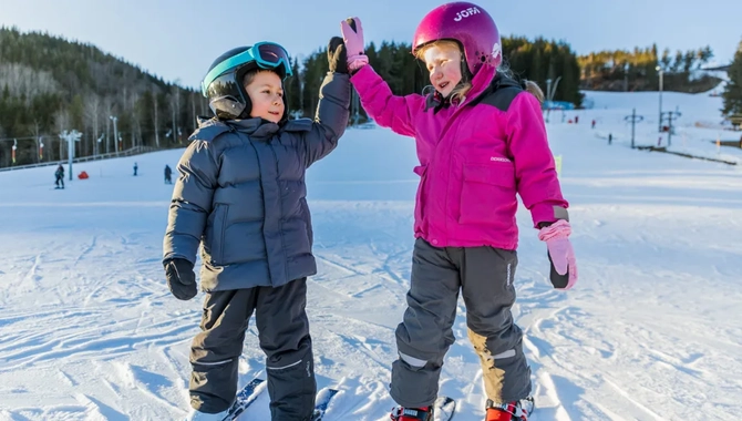 Några barn som står på toppen av en snötäckt sluttning.