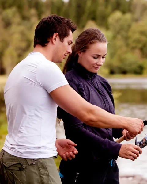 En man  som förklarar hur man håller ett fiskespö för en kvinna vid en sjö.