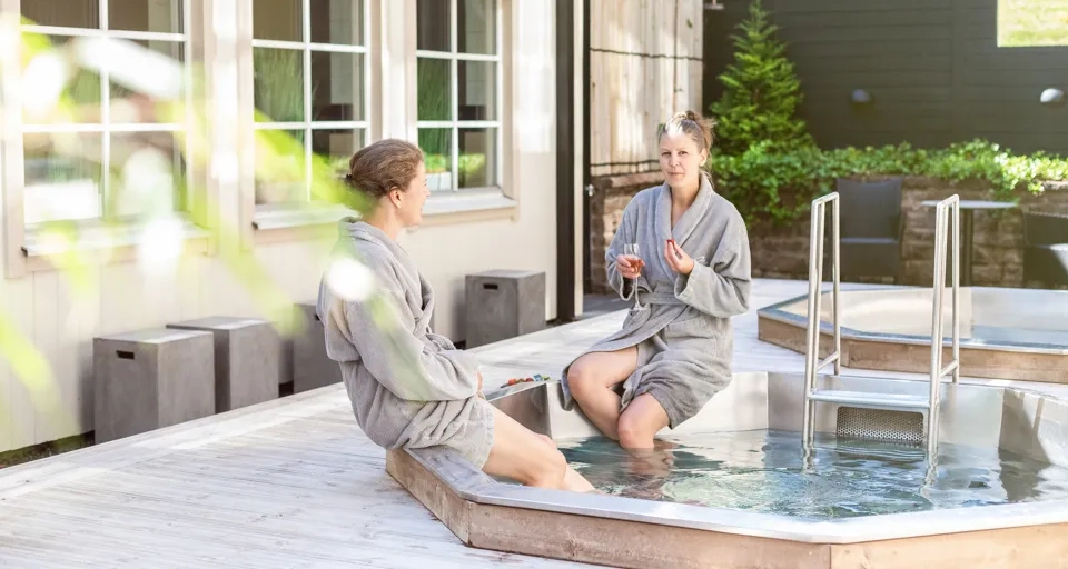 Två kvinnor som sitter med morgonrockar vid en utepool.