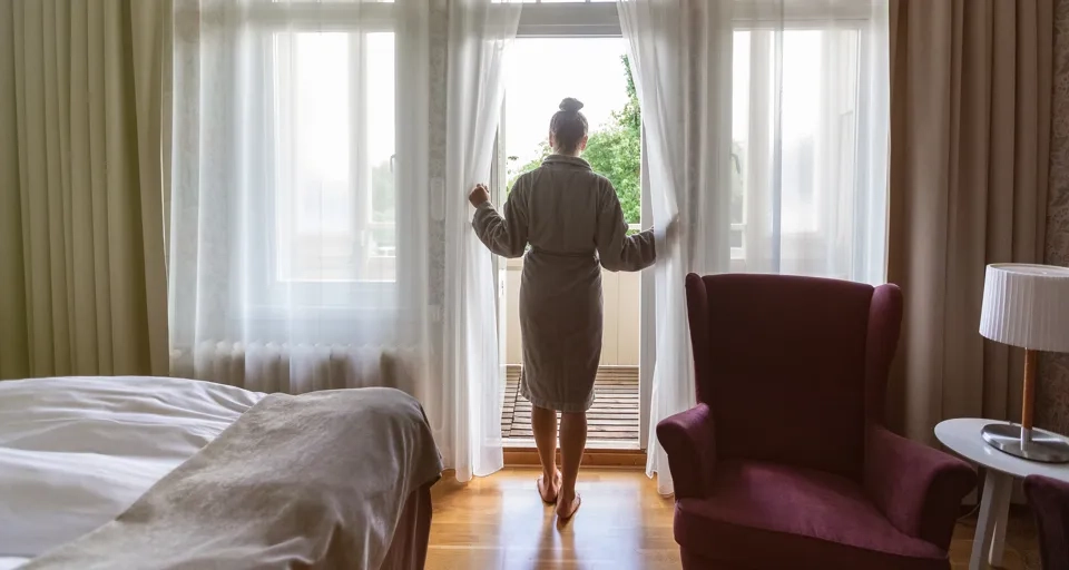 Kvinna i morgonrock står i dörröppningen till balkongen på hotellrummet.