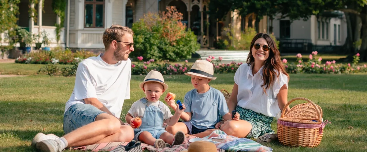 En familj sitter på gräset framför ett hus.