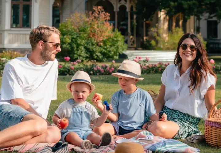 En familj sitter på gräset framför ett hus.