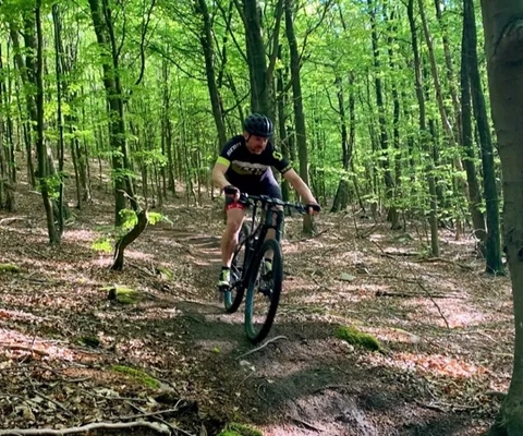 En mann som sykler på terrengsykkel gjennom en skog.