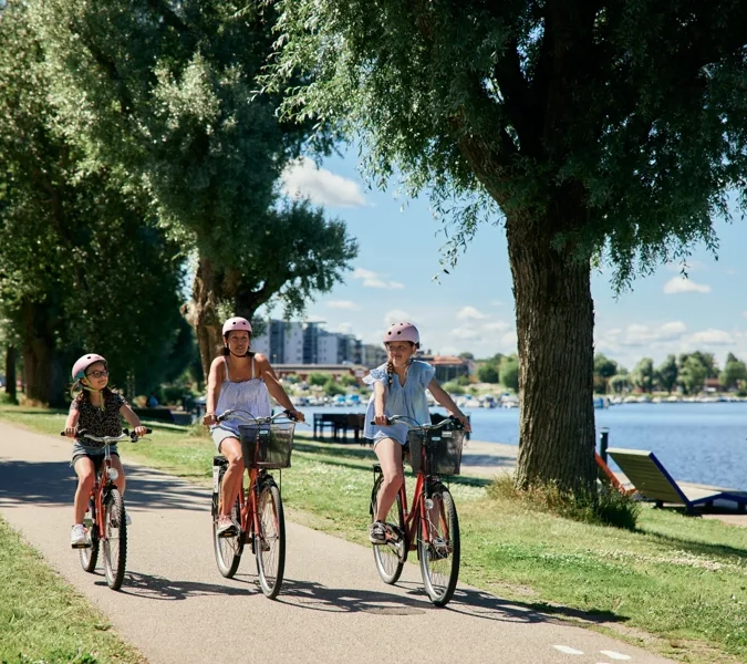 En gruppe mennesker som sykler nedover et fortau ved siden av en innsjø.