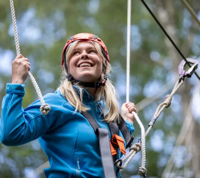 En kvinne i blå jakke henger i et tau.