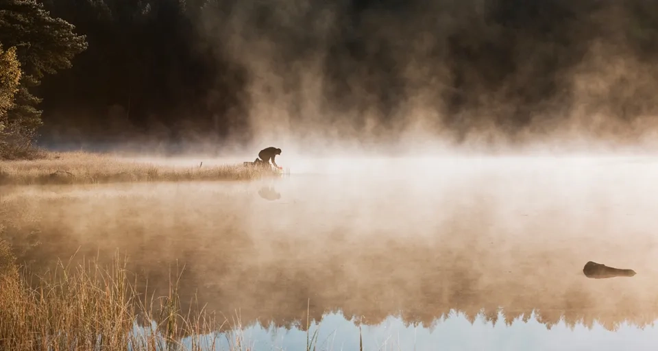 A foggy lake with a dog in the distance.