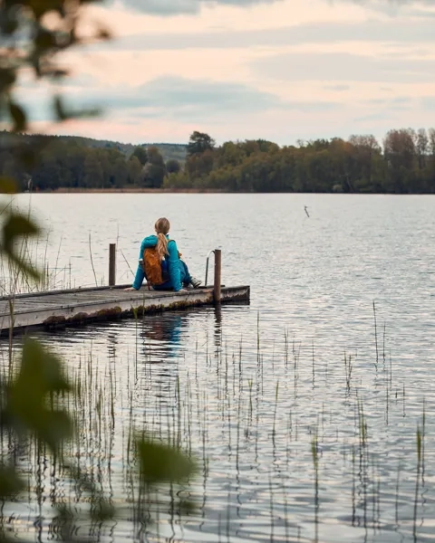 En person sitter på en brygga vid en sjö.