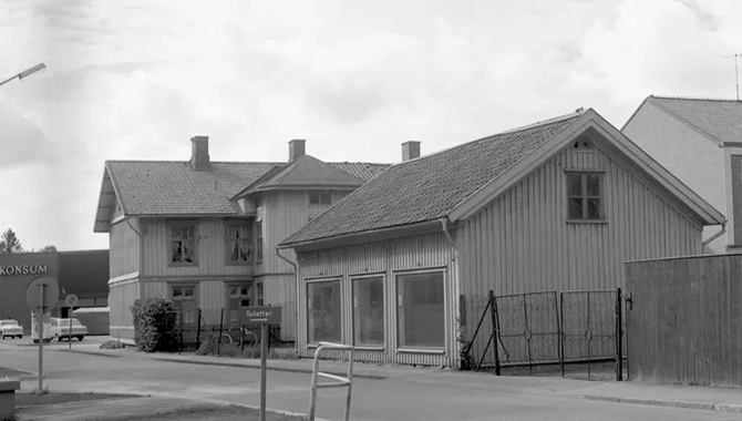 En väg som svänger till vänster. Vid sidan av vägen står några hus med stora skyltfönster.