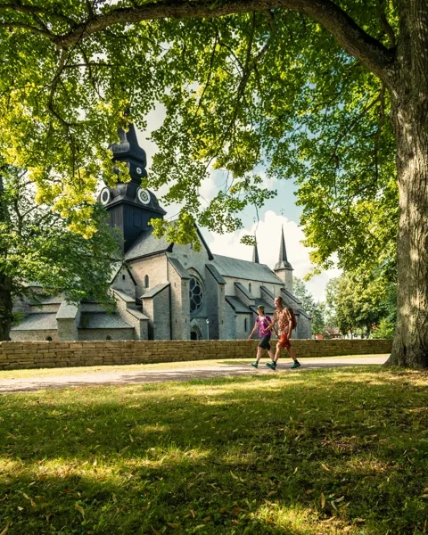 Två personer vandrar på en asfalterad promenadväg. I bakgrunden syns Varnhems klosterkyrka.