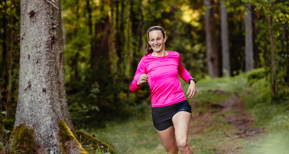En kvinna i rosa tröja springer i skogen.