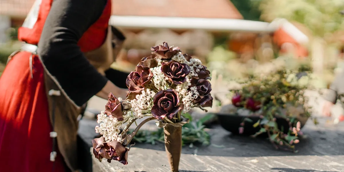 En kvinna i röd klänning arrangerar blommor på ett bord.