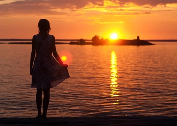 En kvinna står på en strand och tittar på solnedgången.