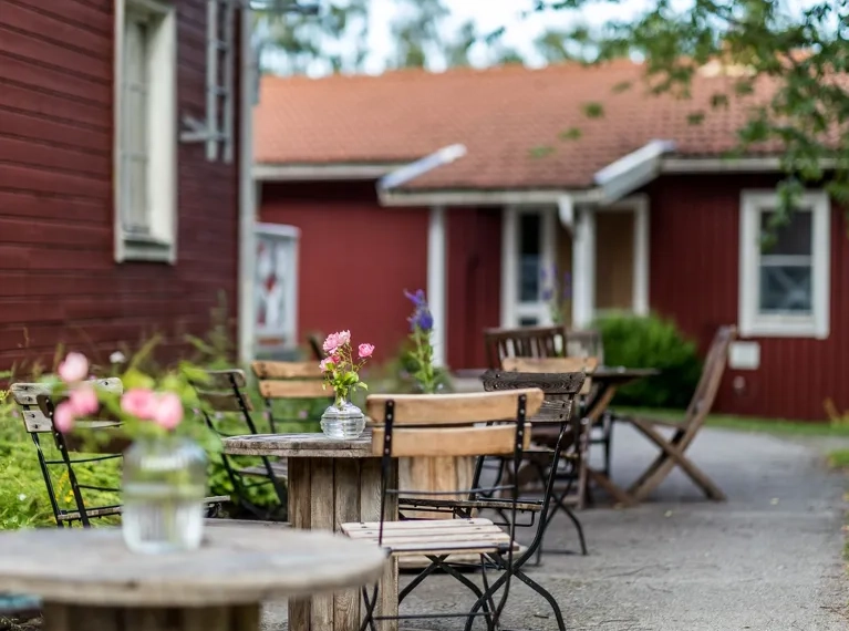 Röda hus på en gård med bord och stolar på gruset