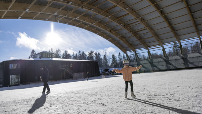 En flicka som står på isbana med utsträckta armar.