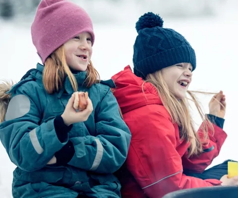 Familj som grillar i vinterlandskapet på Billingen.Två flickor äter korv och skrattar.