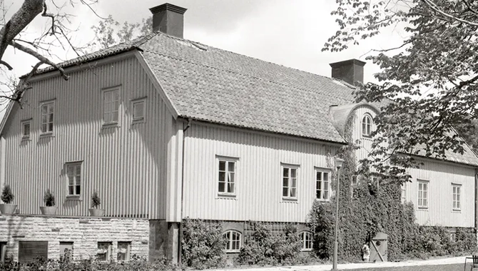Vit stor byggnad, träd och en gräsplan i förgrunden.