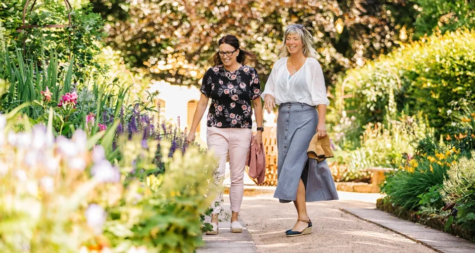 Två kvinnor går längs en stig i en trädgård.