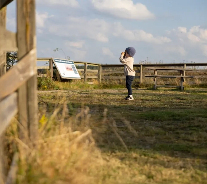 en pojke står och spanar med en kikare ute i naturen.