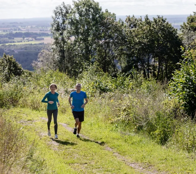 Man och kvinna som springer på ett motionsspår med vacker utsikt över landskapet i bakgrunden.