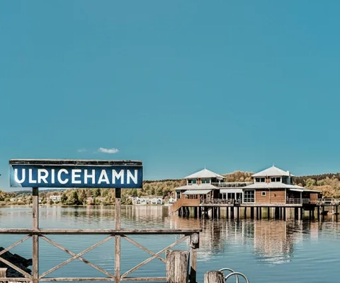 Vy över sjön Åsunden med Ulricehamns Kallbadhus. En skylt med Ulricehamn i förgrunden.