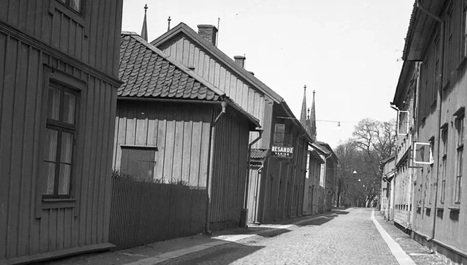 En kullerstensgata går förbi flera byggnader.  Solen skiner.