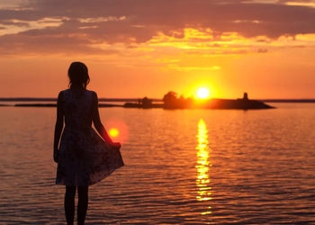 En kvinna står på en strand och tittar på solnedgången.