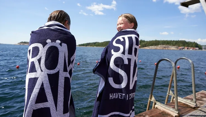 Två barn som står på en badbrygga, inlindade i blåvita badlakan. 