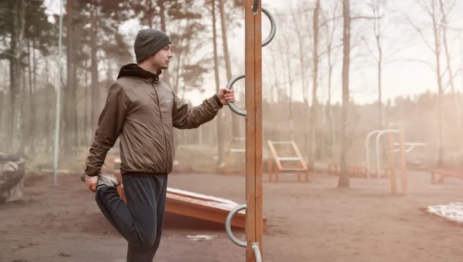 En man håller i en stolpe och stretchar i ett utegym.