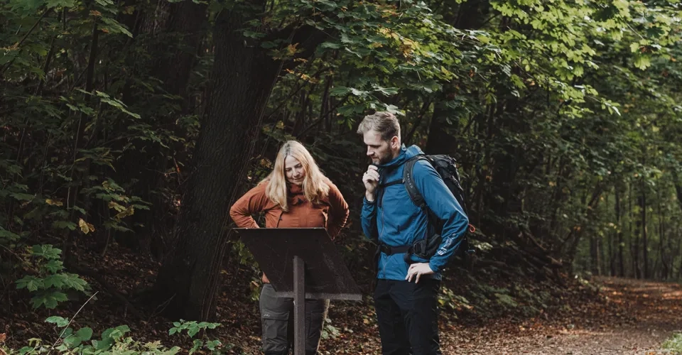 En kille med blå jacka och kvinna i orange jacka står på en stig och läser en skylt.
