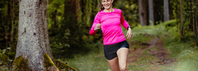 En kvinna i rosa tröja springer i skogen.