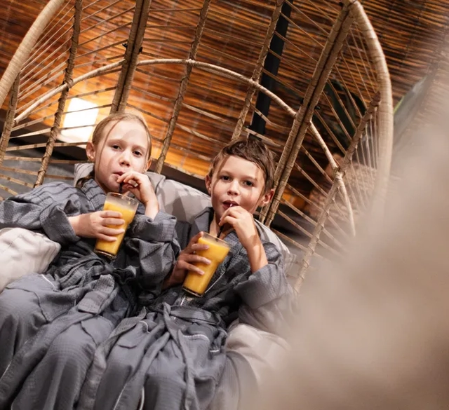 En flicka och en pojke dricker varsin smoothie i morgonrockar i korgstol på relaxavledning