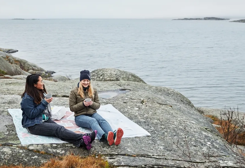 Två kvinnor sitter på en sten intill ett vattendrag.