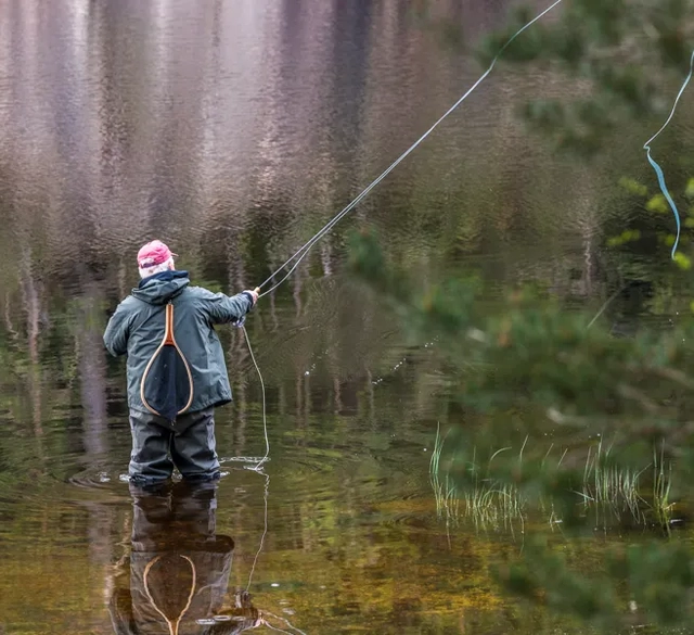 En person står i vattnet och fiskar i Stockasjöarna i Öxabäck. Det speglar sig i vattnet.
