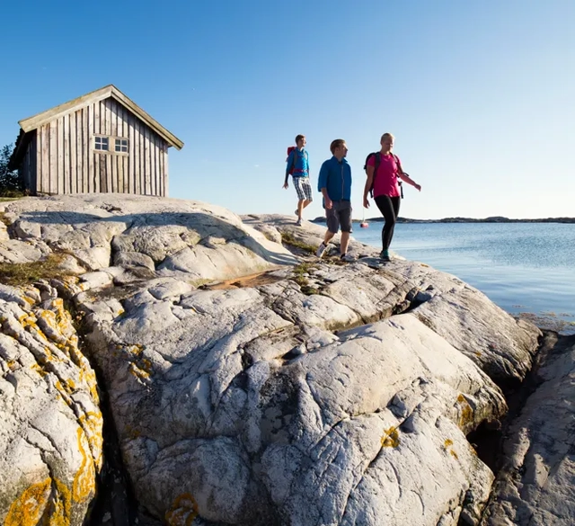 Sällskap vandrar på klipporna vid sjöbod