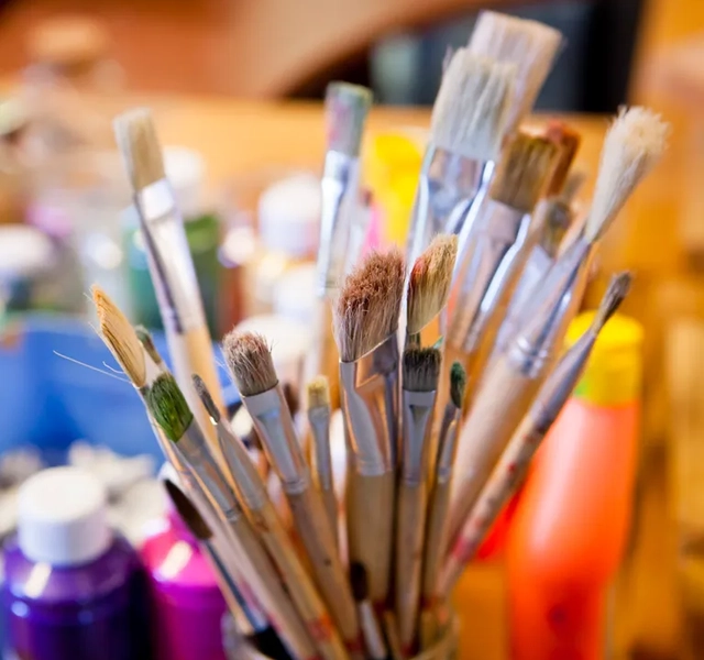 En kopp fylld med massor av färg och penslar.