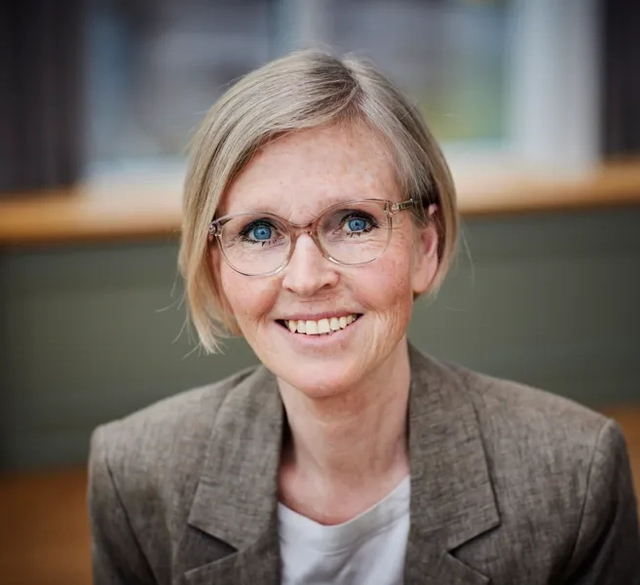 En kvinna med glasögon som ler mot kameran.