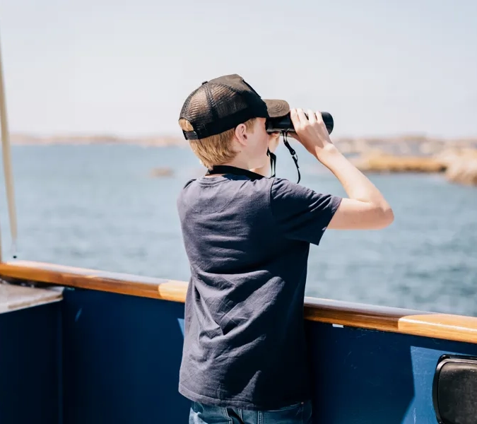 A boy looking through binoculars on a boat.