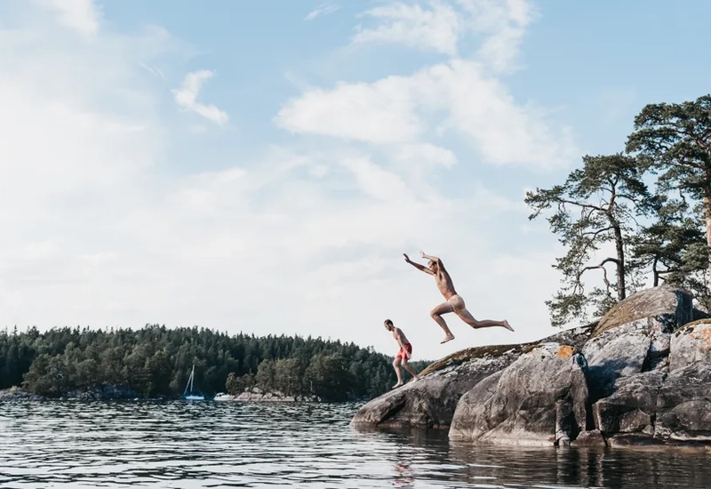 Två personer som hoppar från en klippa ner i vattnet.